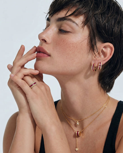 Model trägt burgunderrote Creolen, Halskette und Ring in Gold